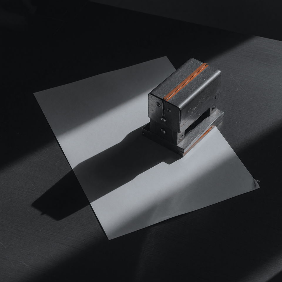 A metal hand stamp standing on a pale sheet of paper, casting a long shadow.
