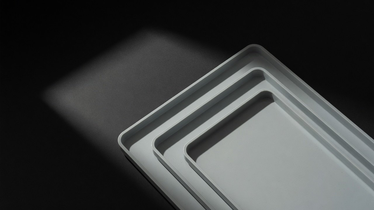 Three shallow pale trays of increasing depth nested together on a dark surface.