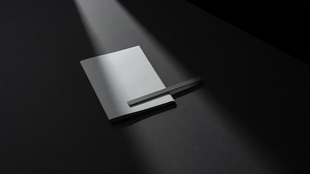 A closed pale folder squared on a dark surface with a thin steel rule laid across it.