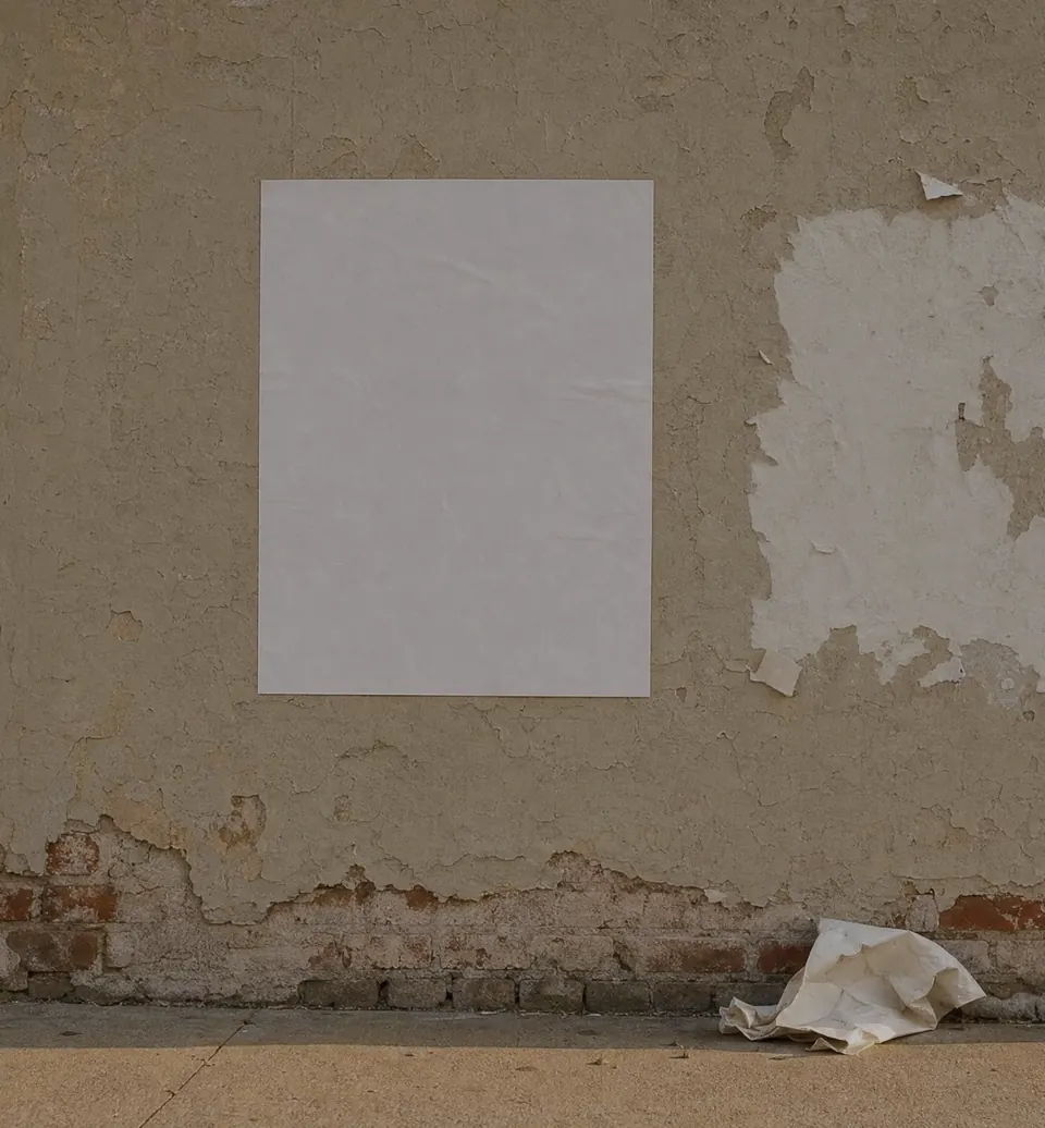 A fresh blank notice pasted on a weathered wall, next to the torn scar where an older one was pulled down, with the crumpled sheet lying on the pavement below.